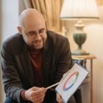 Adult man explaining a color-coded diagram on a clipboard in a cozy room setting.